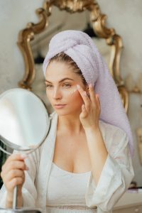 woman holding a mirror and applying eye cream in little dots under her left eye