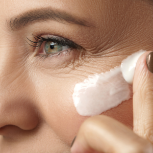 A closeup of a person's face as they apply some eye cream on their cheek bone